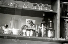 Zdjęcie półki, na której znajdują się książki, kieliszki i alkohol w małych i większych butelkach, Białystok, druga połowa lat 70. XX w., fot. ze zbiorów Andrzeja Trzcińskiego