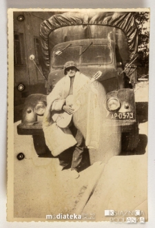 Mężczyzna na tle ciężarówki, w hełmie, z gitarą i kołdrą na ramionach, PGR Kociołek, 1973 r.