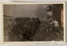 Grupa mężczyzn stojąca w rzędzie przed dwoma osobami, na wieczornej zbiórce po pracy