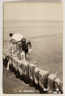 Młodzież przy drewnianych palach na brzegu morza, Ustka, 1979 r.