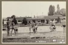 Dwaj młodzi mężczyźni pozujący do zdjęcia w kąpielówkach przed odkrytym basenem