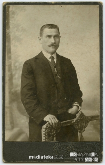 Portret mężczyzny w garniturze, oparty o poręcz. Zdjęcie wykonane w atelier fotograficznym Modern W. Menszikowa, Borisoglebsk