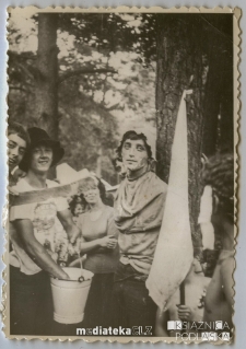 Harcerze z białą flagą i wiadrem na tle obozowiska