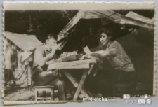 Dwoje harcerzy siedzących przy stole przed namiotem, pocz. lat 70-tych XX w.