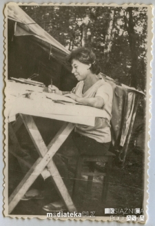 Kom. obozu Jadwiga Telecka notująca coś przy stole, lata 70. XX w.