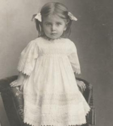 Mała dziewczynka w bialej sukience stojąca na fotelu