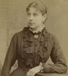 Kobieta w sukni z żabotami, oparta o stolik na którym leży album