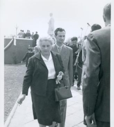 Starsza pani i towarzyszący jej mężczyzna, za nimi trybuna i pomnik Marcelego Nowotki