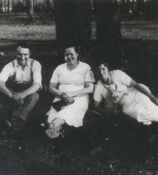 Dwie kobiety i mężczyzna siedzą pod drzewem na trawie