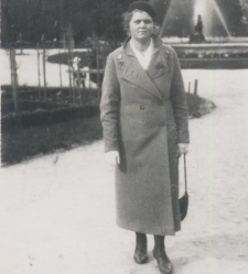 Kobieta w płaszczu i berecie na tle fontanny w parku