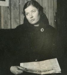 Młoda kobieta w ciemnym ubraniu czyta gazetę "Bialystoker Zeitung" siedząc na kanapie