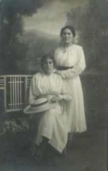 Dwie kobiety w białych sukienkach, jedna z białym kapeluszem w atelir fotograficznym