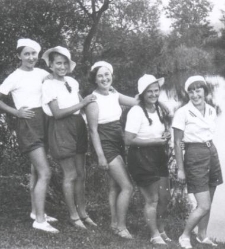 Pięć dziewcząt w krótkich spodenkach i w białych bluzkach na brzegu wody